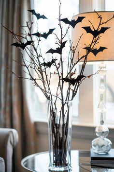 a glass vase filled with branches and bats on top of a table next to a lamp