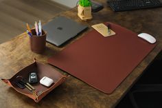 a wooden desk topped with a laptop computer next to a mouse pad and pen holder