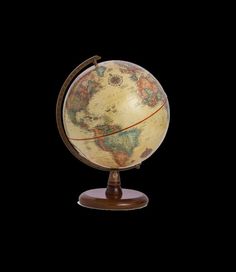 an old world globe on a stand against a black background with clipping for text