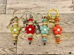 four keychains with different colored beads and charms on top of a wooden floor