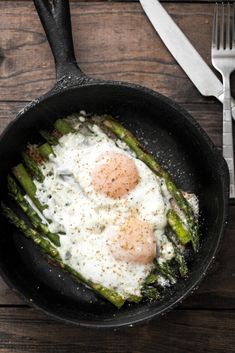 an egg and asparagus frying in a skillet on a wooden table