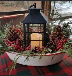 a candle in a bowl with pine cones and berries