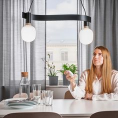 a woman sitting at a table in front of a window holding a cup and looking up