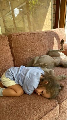 a young child laying on top of a couch next to a dog sleeping on the floor