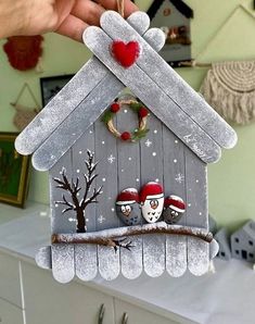 a person holding up a birdhouse ornament with two birds on the roof