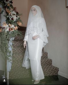 a mannequin wearing a white wedding dress and veil next to a flower arrangement