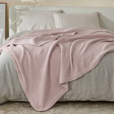 a bed with a pink blanket on top of it and pillows in front of it