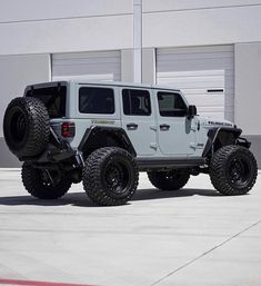 a white jeep is parked in front of a building with two large tires on it