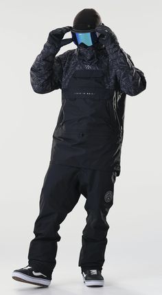 a man in black snowsuit and goggles standing with his hands on his head