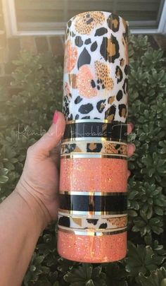 a hand holding up an orange and black tumbler cup with leopard print on it