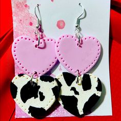 two heart shaped cow print earrings on top of a card with pink and black polka dots