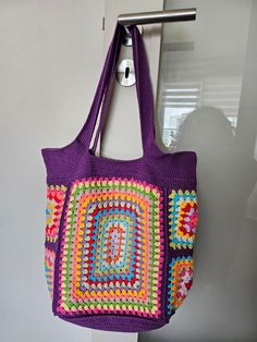 a purple crocheted bag hanging from a hook on a door way with a window in the background