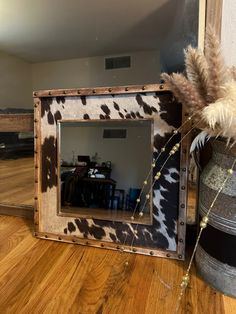 a cow print mirror sitting on top of a wooden floor next to a metal bucket