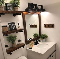 a white toilet sitting under a bathroom mirror next to a sink and shelf with potted plants