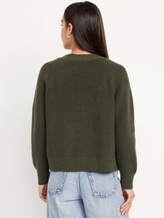 a woman wearing a green sweater and blue jeans is looking at the back of her jacket