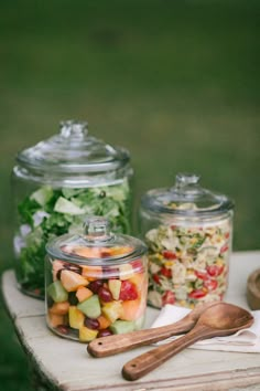 three glass jars filled with food sitting on top of a wooden table next to spoons