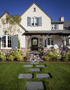 a white house with blue shutters on the front and side windows, grass walkway leading up to it