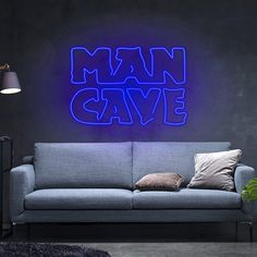 a couch sitting in front of a neon sign that says man cave on the wall