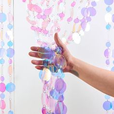 a hand is reaching out from behind some colorful beads on a white background with pink, blue and purple colors