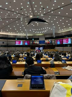 an auditorium full of people sitting at desks with laptop computers in front of them