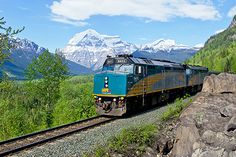 a train is traveling through the mountains with snow capped peaks in the backgroud