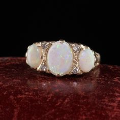 three opal and diamond ring sitting on top of a red velvet surface