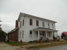 an old white house sitting on the side of a road next to a red fire hydrant