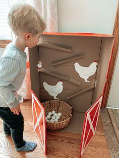 a little boy standing in front of a chicken coop ball drop box filled with eggs