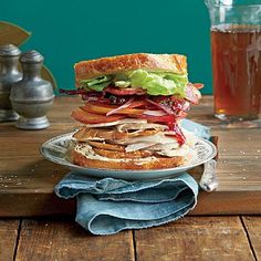 a sandwich with meat, lettuce and tomato on a plate next to a glass of tea