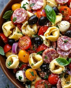 a pasta salad with tomatoes, olives, mozzarella and basil in a brown bowl