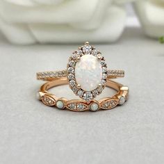 a white opal and diamond ring set on top of a table with flowers in the background