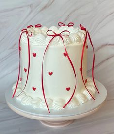 a white cake with red ribbon and hearts on it