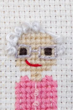 a crocheted doll with glasses on it's face is shown in pink and white