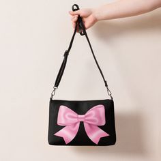 Jump into the pink bow aesthetic and coquette trend with this versatile pink bow crossbody bag with a black background. It has a modern and playful feel, which makes this handbag a great accessory and a perfect gift for every occasion. It's made of premium faux leather and features dark gray hardware. Thanks to the zip-top closure and multiple inside pockets, you can keep your essentials secure and organized. Transform this crossbody bag with removable wrist and shoulder straps to style it for d Cute Black Shoulder Bag With Detachable Strap, Pink Shoulder Bag With Bow, Chic Pink Shoulder Bag With Bow, Pink Bow Bag For Daily Use, Pink Shoulder Bag With Bow For Everyday Use, Black Rectangular Bag With Bow, Cute Black Shoulder Bag For Party, Black Party Bags With Bow Detail, Cute Pink Shoulder Bag For Evening