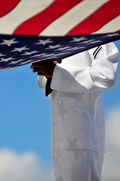 a man holding an american flag in front of his face and body, with the sky behind him