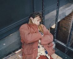 a woman sitting on the ground talking on her cell phone while wearing a red jacket