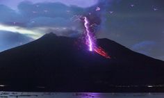 a mountain with lightning coming out of it's top and some water in the foreground