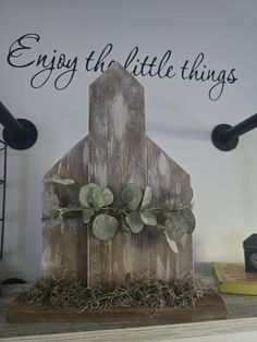 a small wooden house sitting on top of a shelf next to a sign that says enjoy the little things