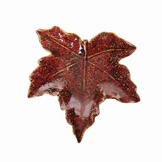 a red leaf shaped brooch sitting on top of a white surface with brown spots