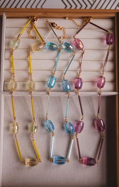 four necklaces in a wooden box with white and blue beads on them, one is multicolored