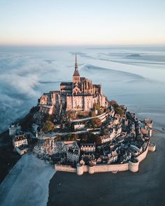 an aerial view of a castle in the middle of the ocean with clouds surrounding it