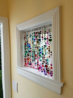 a white frame hanging on the side of a wall filled with colorful beads and chains