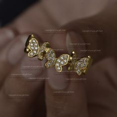 a close up of a person's hand holding an earring with two butterflies on it