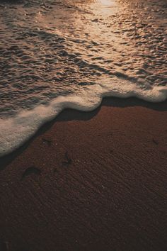 the sun is setting over the ocean with waves coming in and footprints on the sand