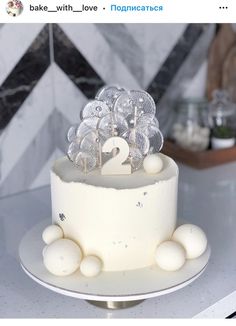 a white cake with frosting balls on top and two candles in the shape of numbers