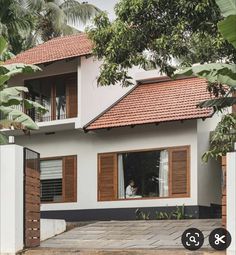 a white house with wooden shutters on the front and side windows, surrounded by greenery