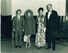 an old black and white photo of four people standing in front of a wall wearing suits