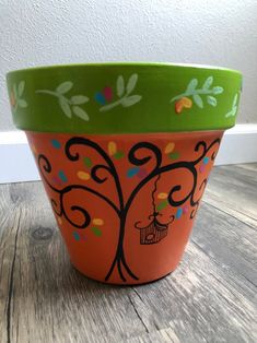 an orange flower pot with a tree painted on the bottom and green trim around it