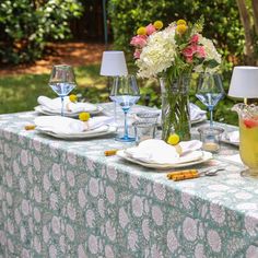 the table is set with glasses, plates and vases filled with flowers on it