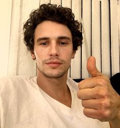 a man with curly hair giving the thumbs up